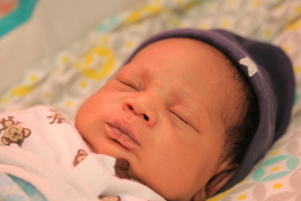 Close-up of a newborn baby sleeping peacefully in warm, colorful blanket.