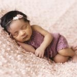 A newborn baby girl peacefully sleeps on a soft pink blanket, embodying innocence and tranquility.