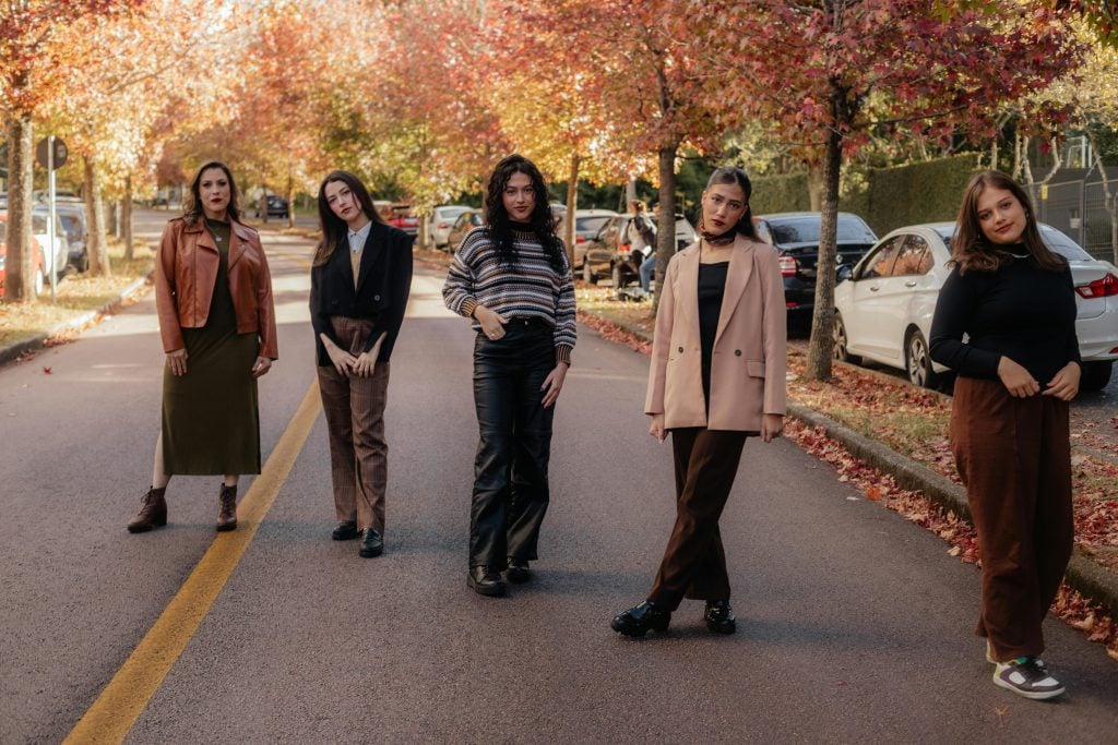 Group of women posing on a city street with autumn foliage, showcasing fashion.