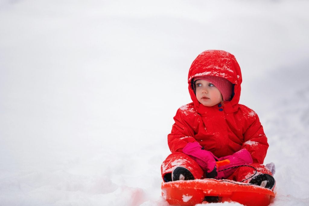 Cute baby in bright red snowsuit playing in the snow on a cold winter day.